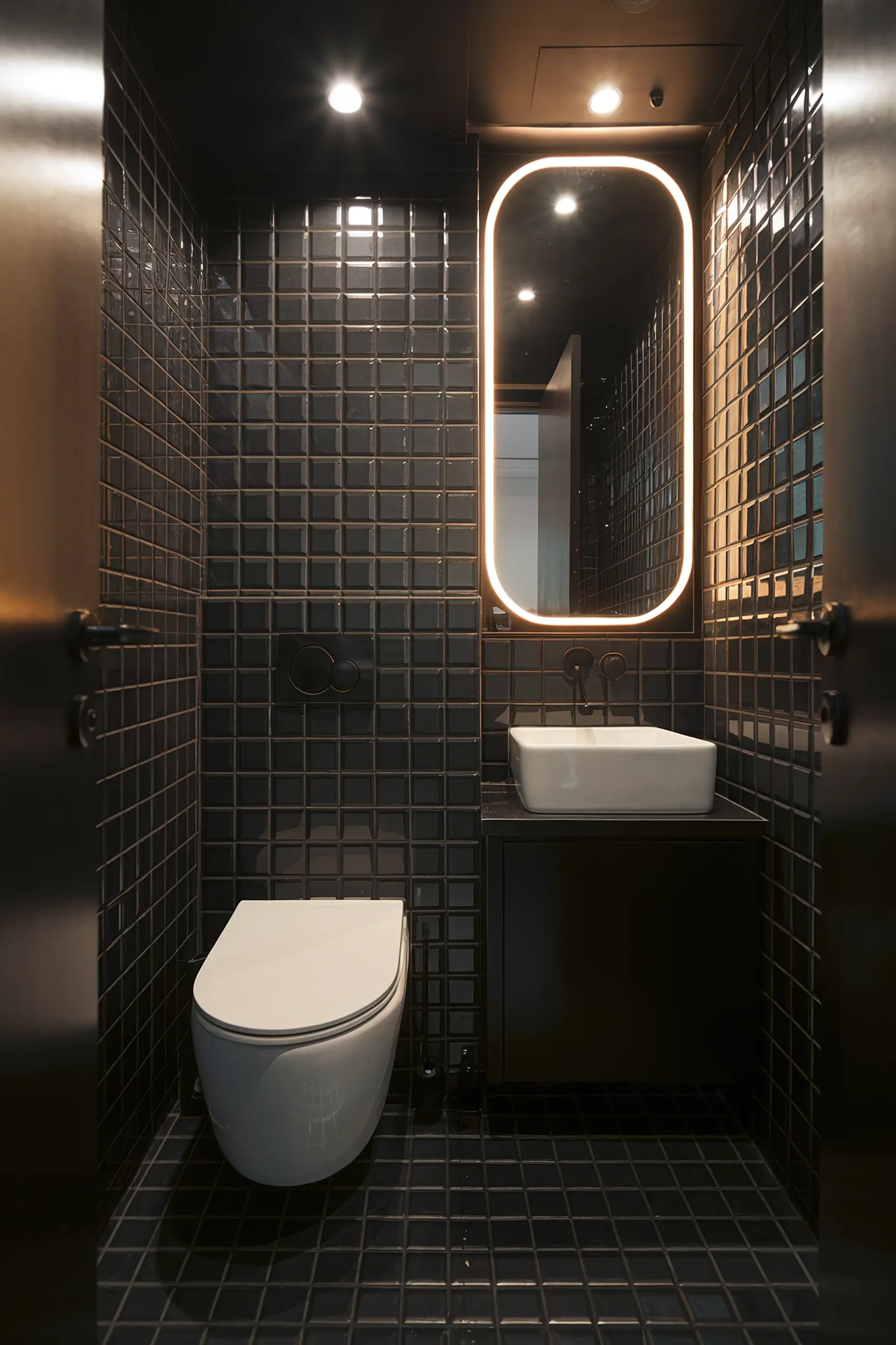 Dramatic small luxury bathroom with dark tones, black tiles, and bold lighting.